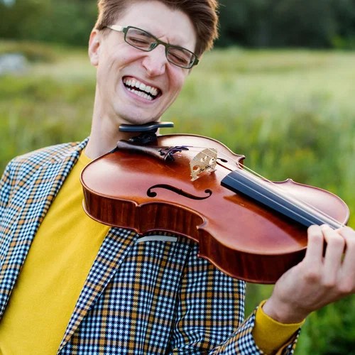Matt grinning with eyes closed, playing viola in a green meadow