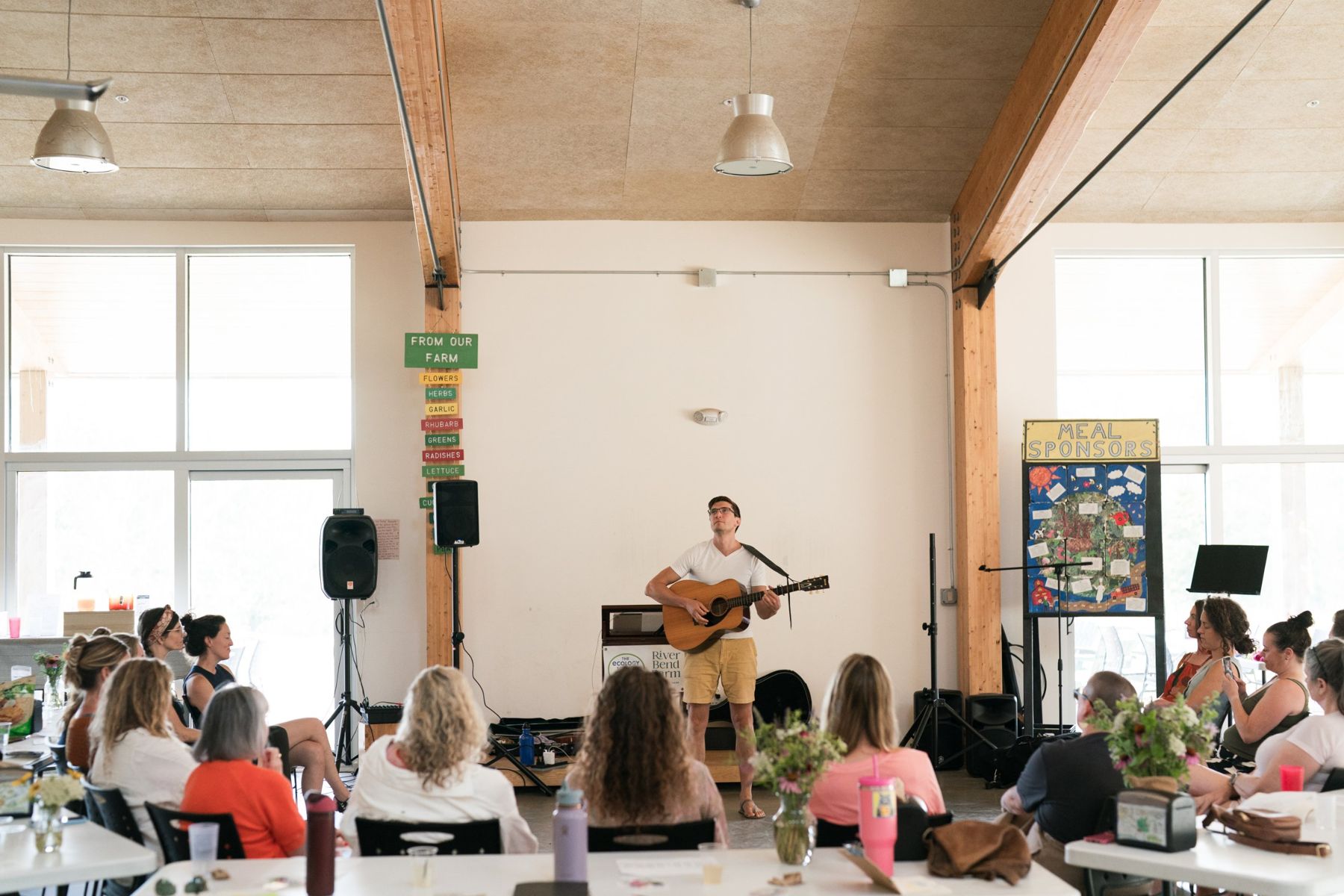 Matt singing with guitar to a full room under wooden beams