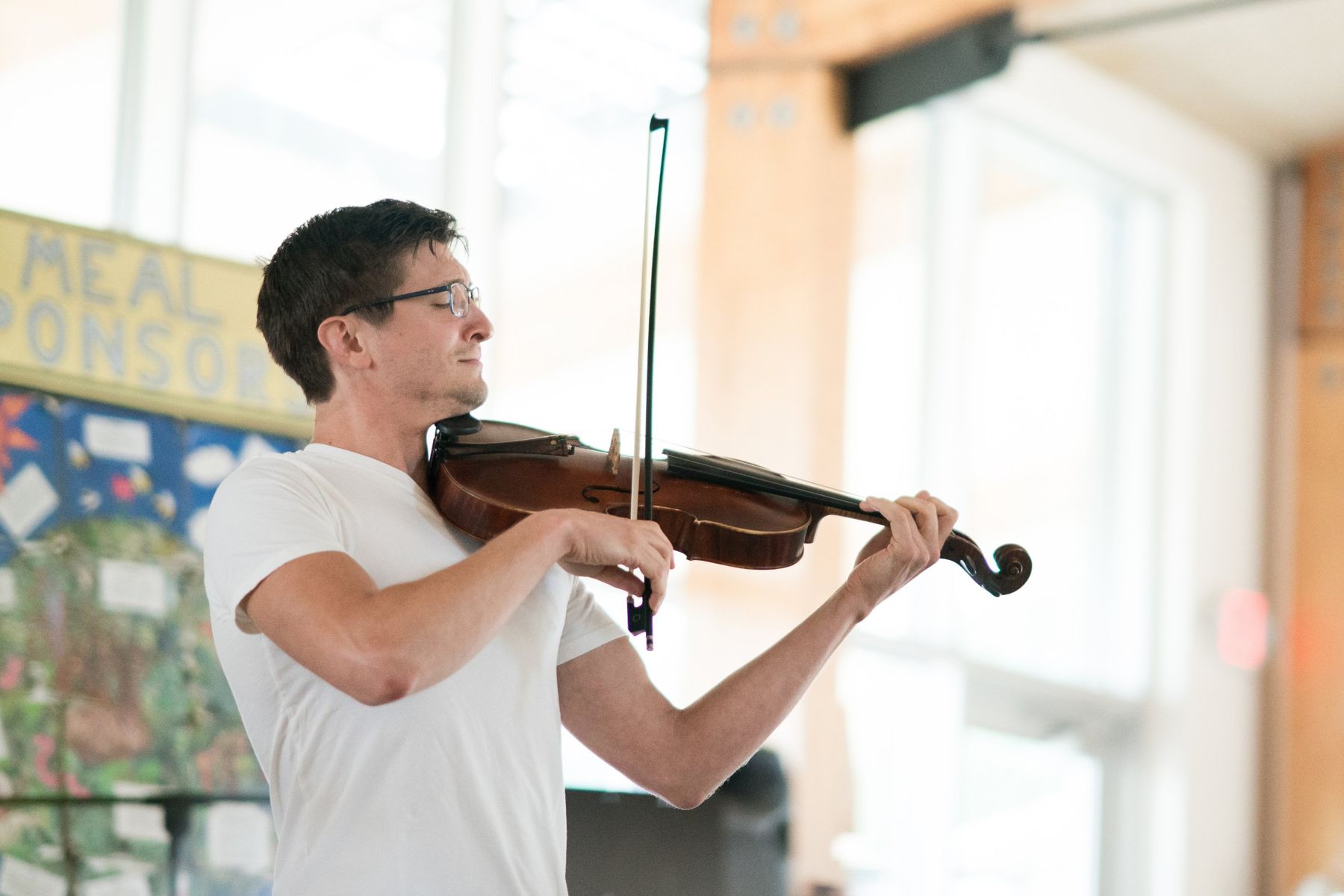 Matt playing viola, eyes closed, bow upright, in a bright wood-beamed hall